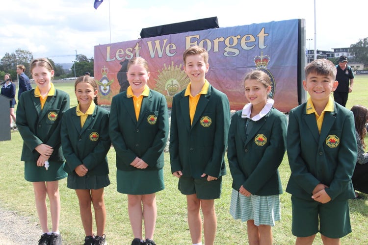 Student leaders standing in front of a Lest We Forget banner .
