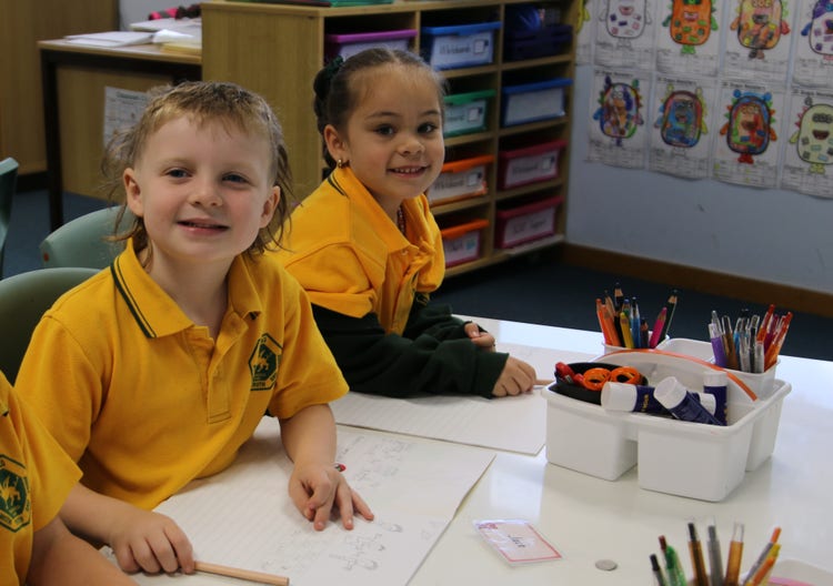 Two students sitting at their desk, smiling at the camera.
